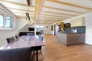 Un comedor amplio con una mesa de madera larga y sillas, una cocina con electrodomésticos modernos y vistas al exterior a través de amplias ventanas.