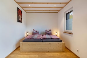 A small bedroom with a wooden bed, two bedside lamps, a window, and a wall-mounted picture.