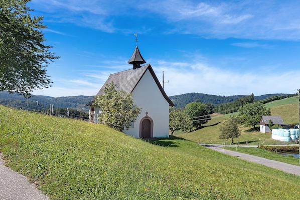 A small church with a steep roof and a bell tower, surrounded by lush green fields and hills.