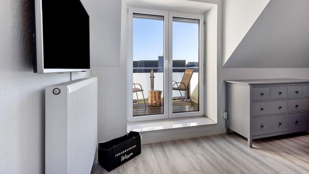 Un apartamento moderno con un ventanal grande, un radiador, un aparador gris y un caja de almacenamiento negra.