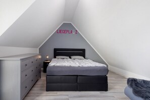 A bedroom with a sloped ceiling, a bed with a black headboard, a dresser, and a nightstand.