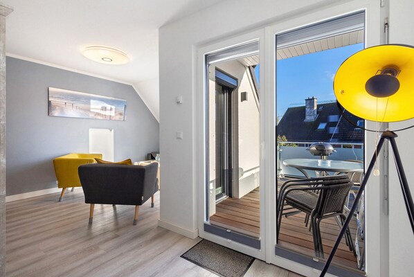 A modern interior with a sliding glass door leading to an outdoor deck, a yellow chair, and a table with chairs.