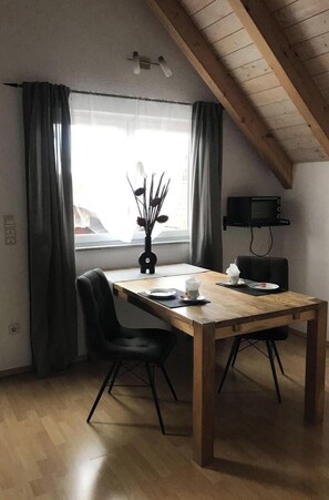 Un coin repas avec une table en bois, des chaises noires, un vase contenant des fleurs séchées et un téléviseur à écran plat fixé au mur.