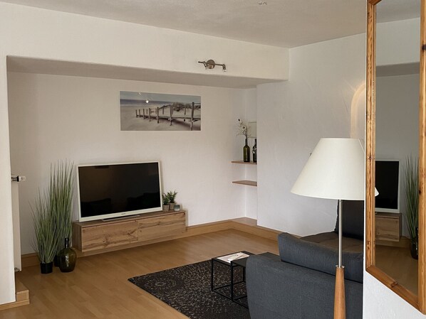 Een moderne woonkamer met een flatscreen televisie, een bank, een lamp en een schilderij aan de muur.