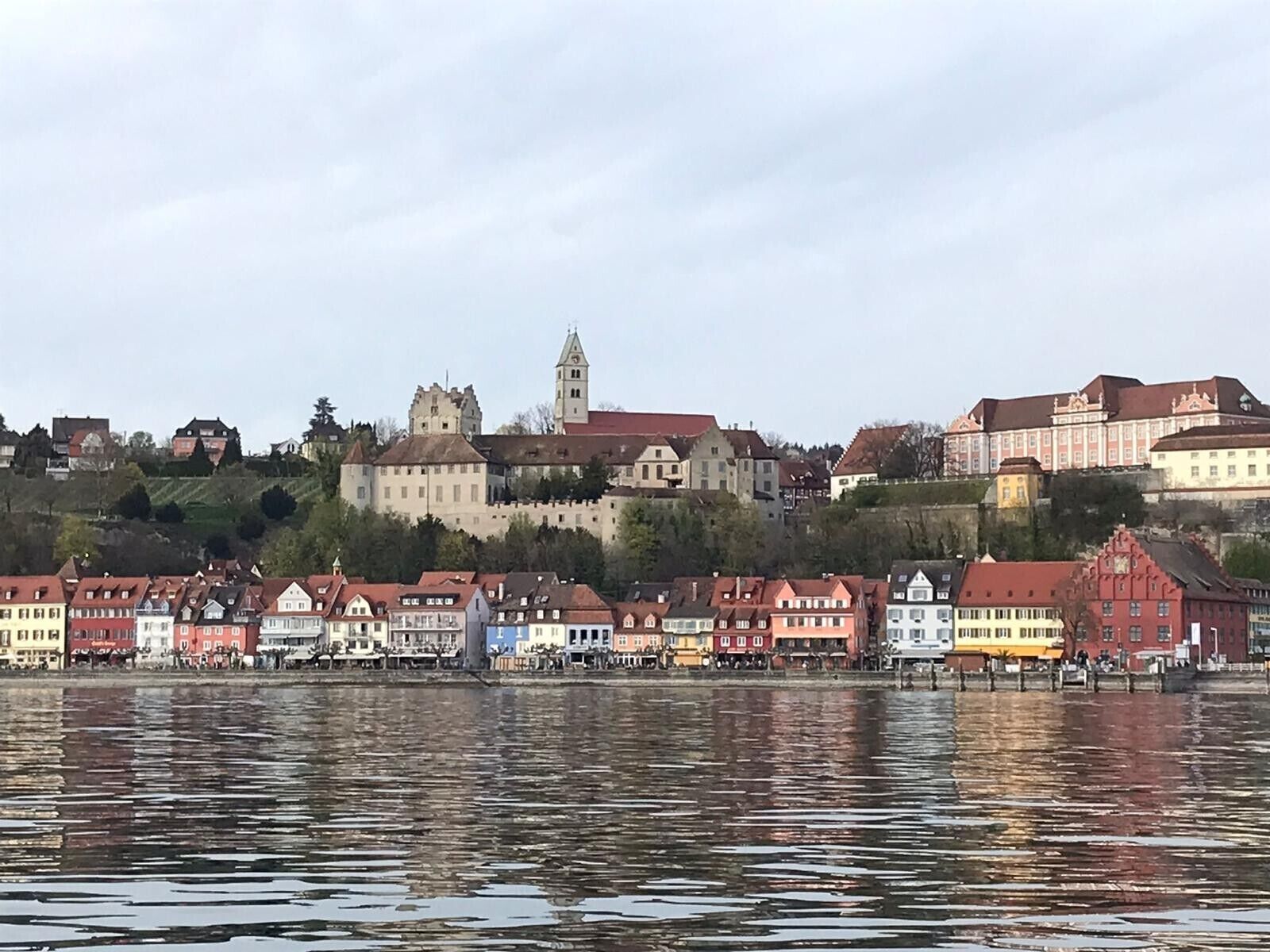 A waterfront cityscape with historic buildings, a prominent church, and a castle on a hill.