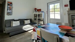 A living room with a sofa, a dining table with chairs, a kitchen area, and a window with a view. - House in a quiet cul-de-sac, within walking or cycling distance of shops and beach.  (Noirmoutier-en-l'Île)