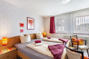 Une chambre d’hôtel avec deux lits, une chaise, une table de chevet, une lampe, une fenêtre avec des rideaux et un radiateur.