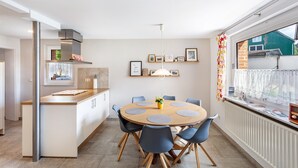 Cozinha moderna com mesa de jantar redonda, cadeiras azuis e janela com vista para uma casa.