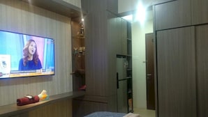 Een slaapkamer met een aan de muur bevestigde televisie, een bed, een kledingkast en een plank met spullen.