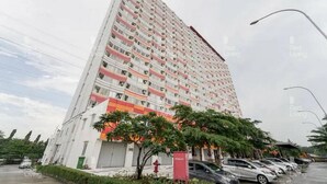 Een hoog appartementencomplex met meerdere balkons, een hekpoort en een parkeerplaats met auto's.