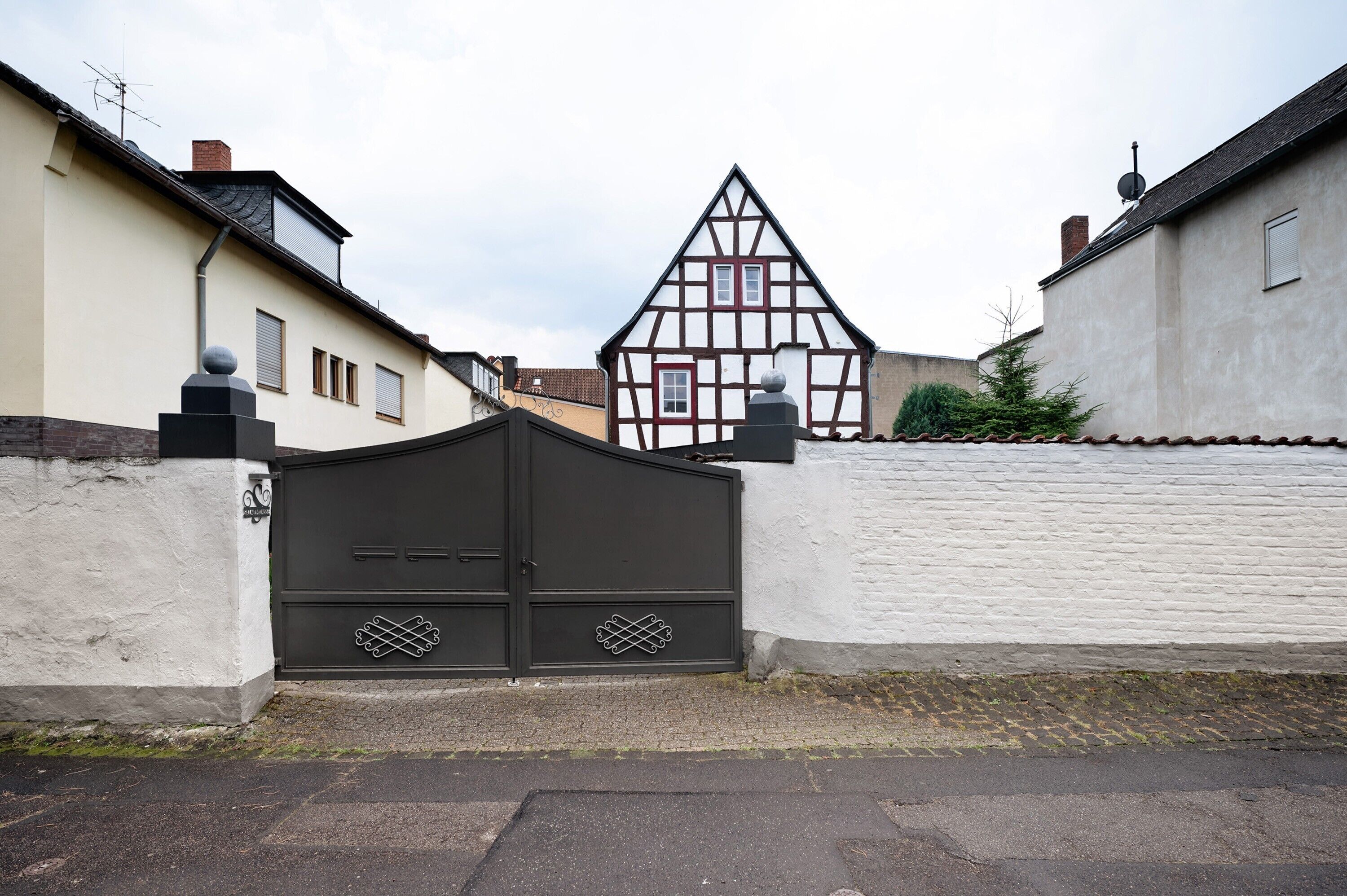 Une entrée fermée par un portail, avec une maison traditionnelle à colombages en arrière-plan.