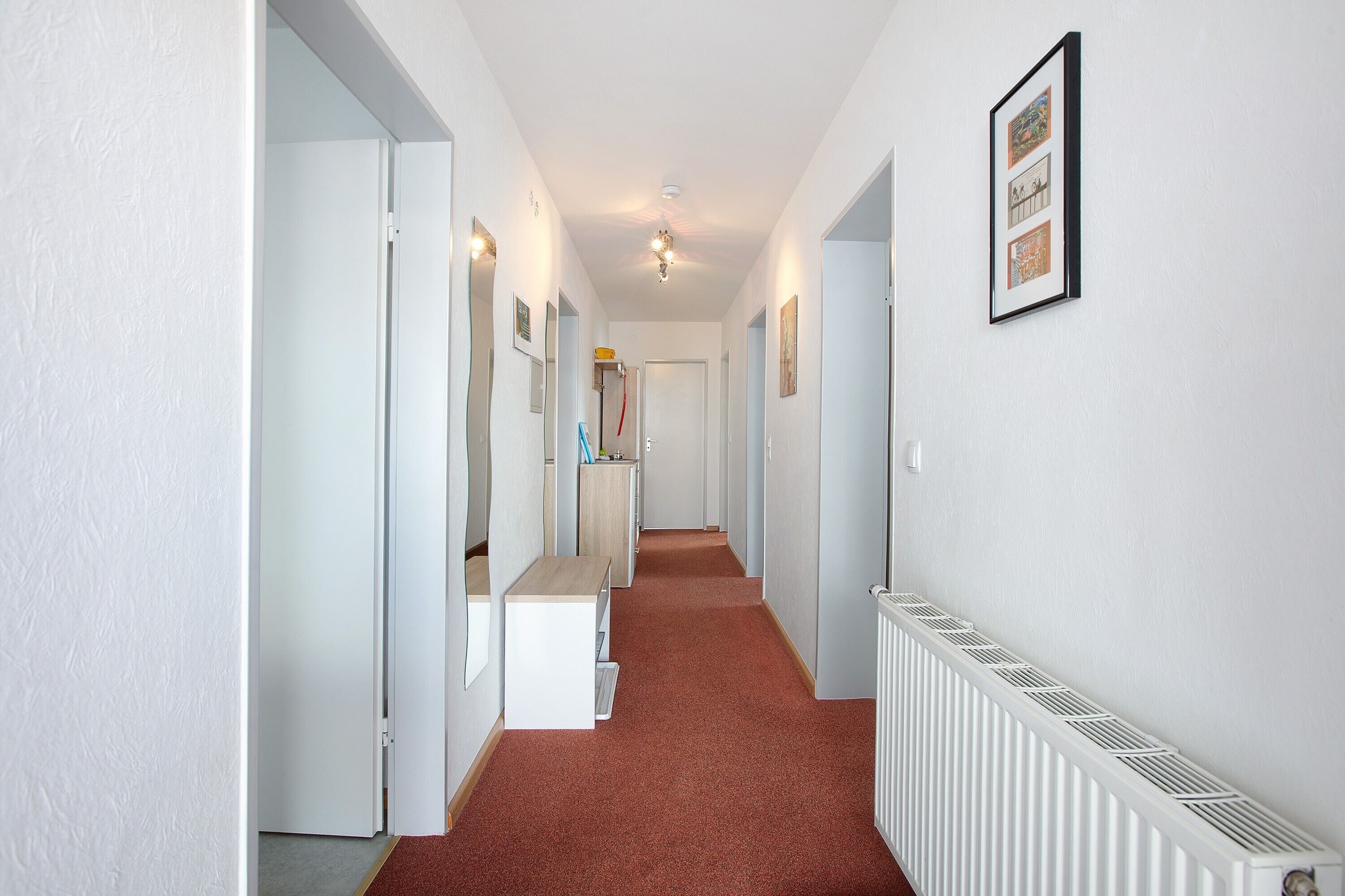 A hallway with a radiator, a bench, and framed pictures on the wall.