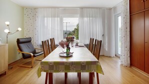 Un comedor con una mesa dispuesta para dos personas, una silla, un florero con flores y vistas al exterior por la ventana.