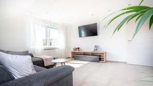 Una sala de estar moderna con sofá, televisión, una mesita y una planta.