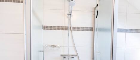 En dusch med glasväggar runt om, ett duschmunstycke som kan hållas i handen, en glasdörr och en handduk på golvet.