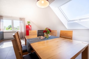 Un comedor con una mesa de madera, sillas, un refrigerador rojo, una ventana con cortinas y un cartel en la pared.