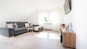 Una sala moderna con un sofá gris, una mesita redonda y un mueble de madera.