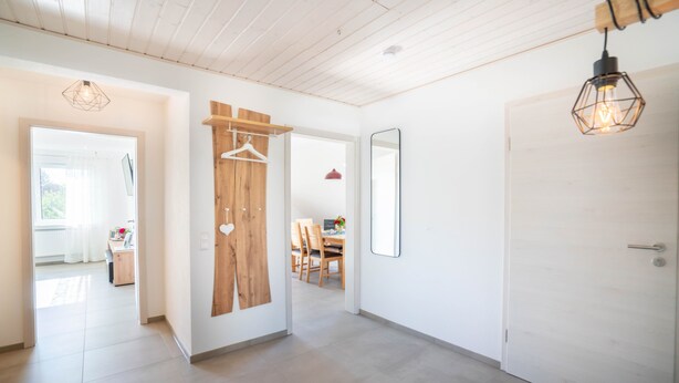 Un interior moderno con una puerta de madera, un perchero, un espejo y una lámpara colgante.