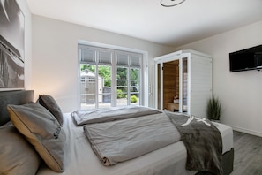 A bedroom with a bed, a wardrobe, a television, and a view through a window.