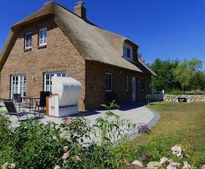 A brick house with a thatched roof, a patio with outdoor furniture, and a garden with flowers.