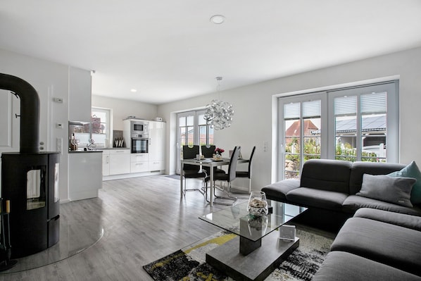 A modern living room with a sofa, a glass coffee table, and a dining area with chairs and a table.