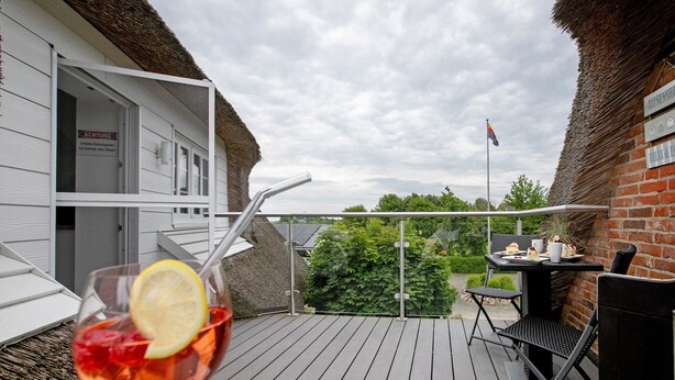 Une terrasse avec une table et des chaises, un verre d’une boisson rouge agrémenté d’une tranche de citron, et un drapeau en arrière-plan.