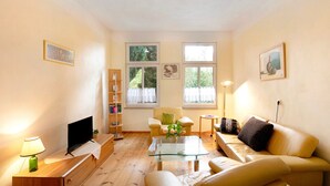 A living room with a glass coffee table, a sofa, a TV, and a bookshelf.