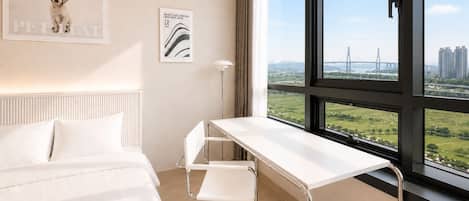 Habitación de hotel con cama, escritorio y un amplio ventanal que ofrece vistas de un puente y edificios.
