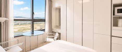 Habitación de hotel con cama, una mesita de vidrio, una silla, televisor y vista a un puente y al paisaje urbano.