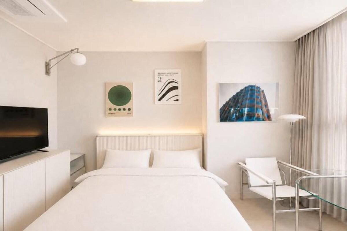 Een hotelkamer met een bed, een bureau, een stoel, een televisie en kunstwerken aan de muur.