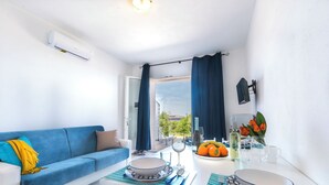 A modern living room with a blue sofa, a dining table set with plates, glasses, and a bowl of fruit. - Trilo Vista Mare-residence La Smeralda (Castelsardo)