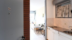 A modern kitchen with white cabinets, a stainless steel countertop, and a window with curtains. - Chiasso Apartments (Chiasso)