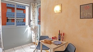 A dining area with a table set for two, a fan, and a window with curtains. - Chiasso Apartments (Chiasso)