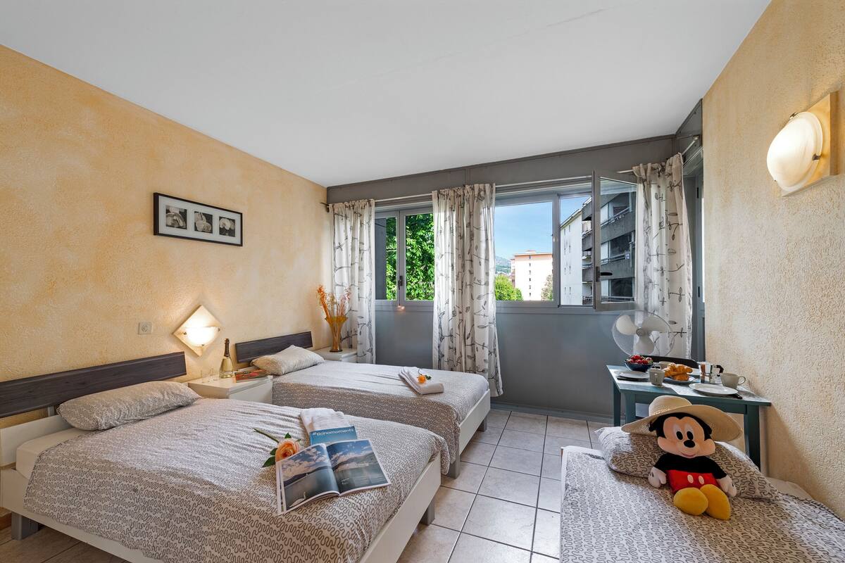 Une chambre d’hôtel avec deux lits, un coin repas et un balcon avec des rideaux.