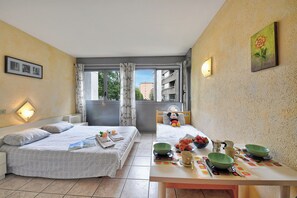 A hotel room with two beds, a dining table with breakfast items, and a view through the window. - Chiasso Apartments (Chiasso)