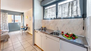 A compact kitchen with a sink, a small refrigerator, and a dining area with a table and chairs. - Chiasso Apartments (Chiasso)