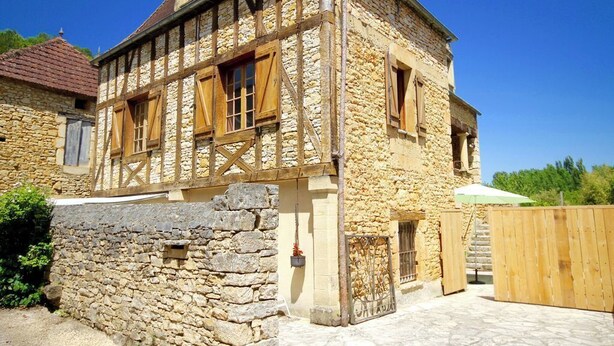 Un bâtiment traditionnel en pierre, avec une structure en bois apparent, un mur de pierre et un portail en bois.