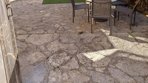 Une terrasse en pierre avec une table et des chaises, un petit parasol et un escalier menant à une terrasse en bois.