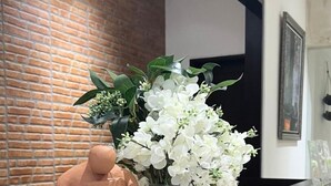 A room with a brick wall, a framed picture, and a vase of white flowers. - Casa Verde Guesthouse (Mengwi)