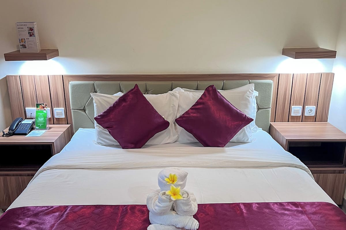 Cama bem arrumada com colcha vermelha, dois travesseiros e arranjo de toalhas com flores.