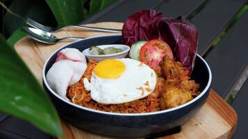 A bowl of food with a fried egg, vegetables, and a piece of meat on a wooden board.