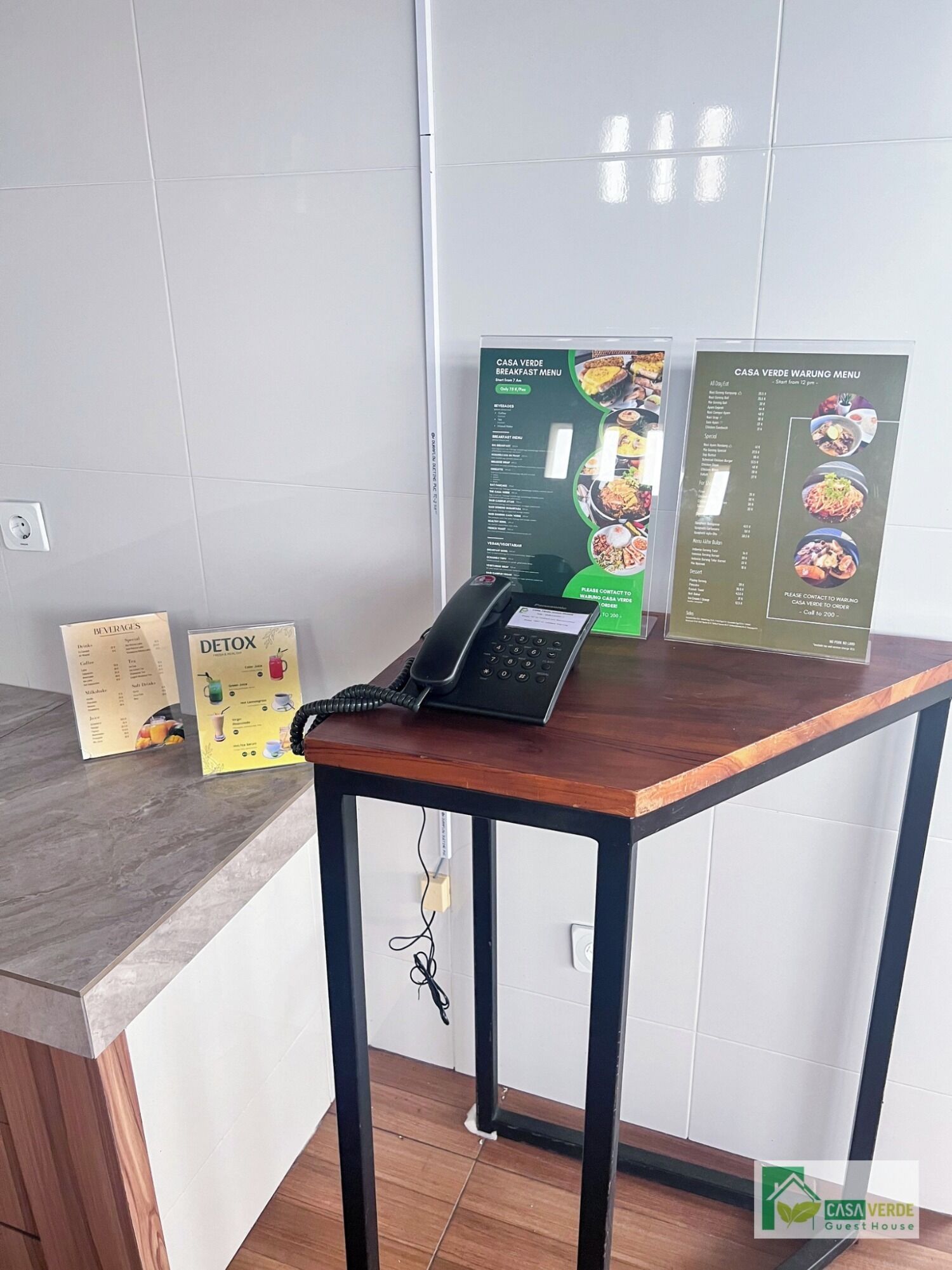 Ein Holztisch mit einem Telefon und einer Menütafel, die Frühstücks- und Warung-Optionen anzeigt.