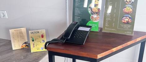 Ein Holztisch mit einem Telefon und einer Menütafel, die Frühstücks- und Warung-Optionen anzeigt.