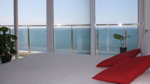 A bedroom with a large window overlooking the sea, a bed with white bedding, and a potted plant. - Stay next to the sea but central to all your need.  (Colombo)