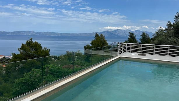 A clear view of a swimming pool with a glass railing, overlooking a body of water and distant mountains.