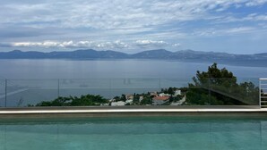 A pool with a view of a calm sea and distant mountains under a partly cloudy sky.