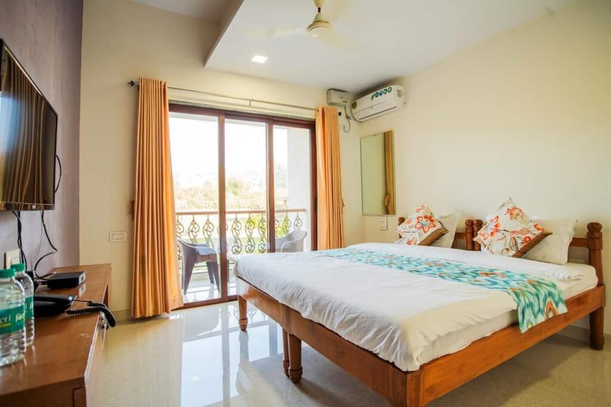 A hotel room with a bed, a desk with a telephone, an air conditioning unit, and a balcony with curtains.