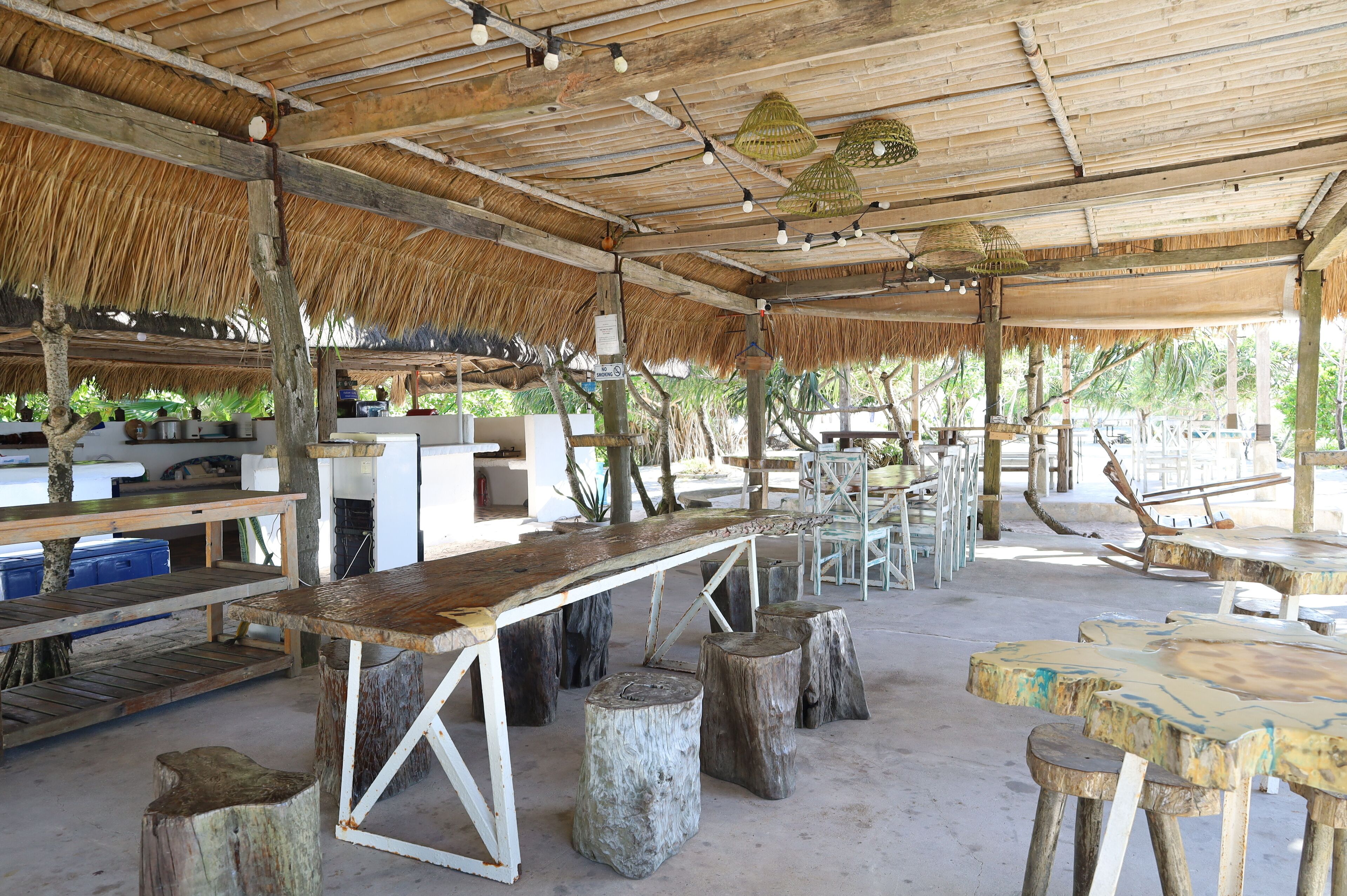 An outdoor dining area with wooden tables and benches, a thatched roof, and a view of the surrounding landscape.
