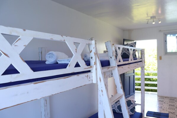 Habitación con literas, una paleta de colores blanco y azul, una ventana con vistas a la vegetación y una puerta que da a un espacio exterior.