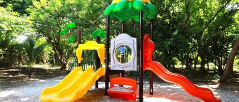 A playground with slides and climbing structures surrounded by trees.